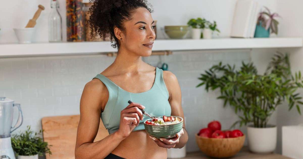Pessoa hidratando-se com um copo d'água ao lado de frutas e vegetais ricos em fibras