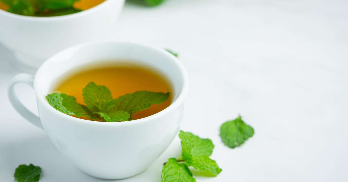 Xícara de chá de hortelã com folhas frescas ao redor