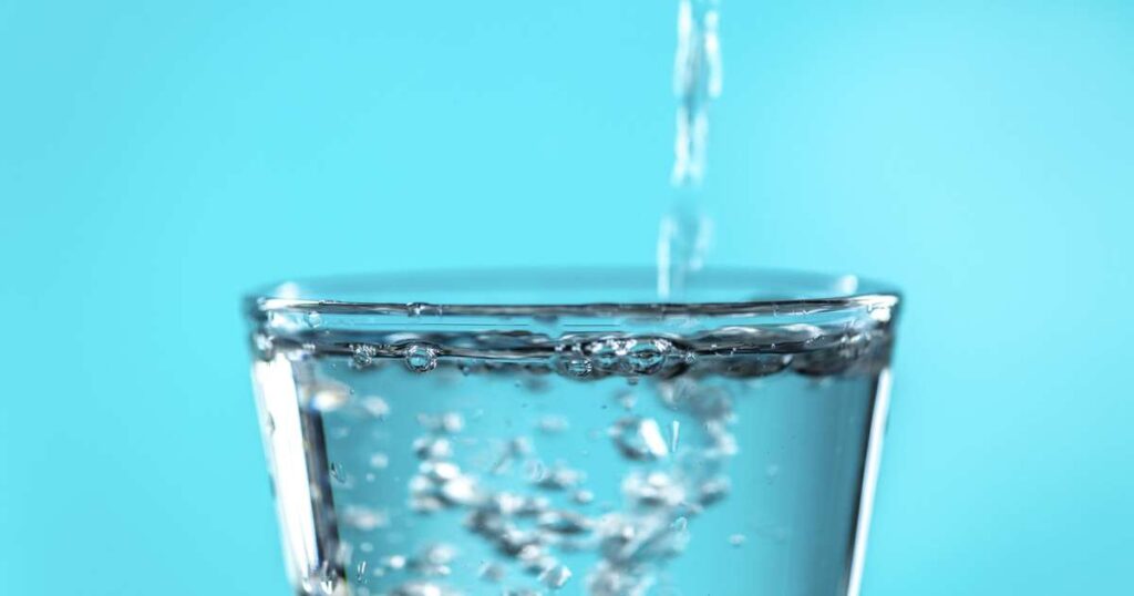 Copo de água com gás com bolhas efervescentes ao lado de fatias de limão