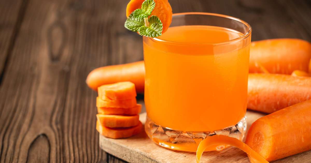 Suco de cenoura em um copo com cenouras frescas ao fundo