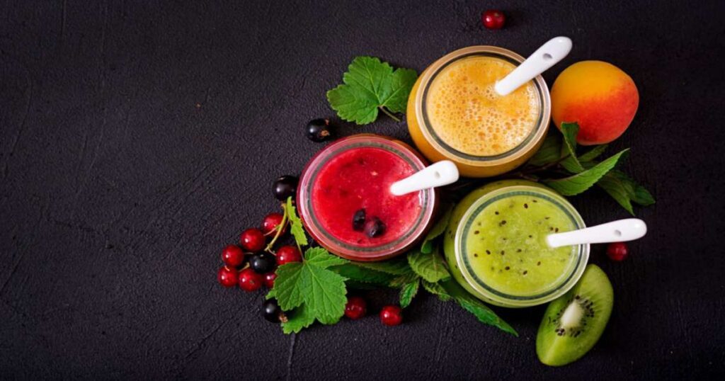 Vários sucos detox coloridos em copos transparentes com ingredientes frescos ao redor, como frutas e folhas verdes.