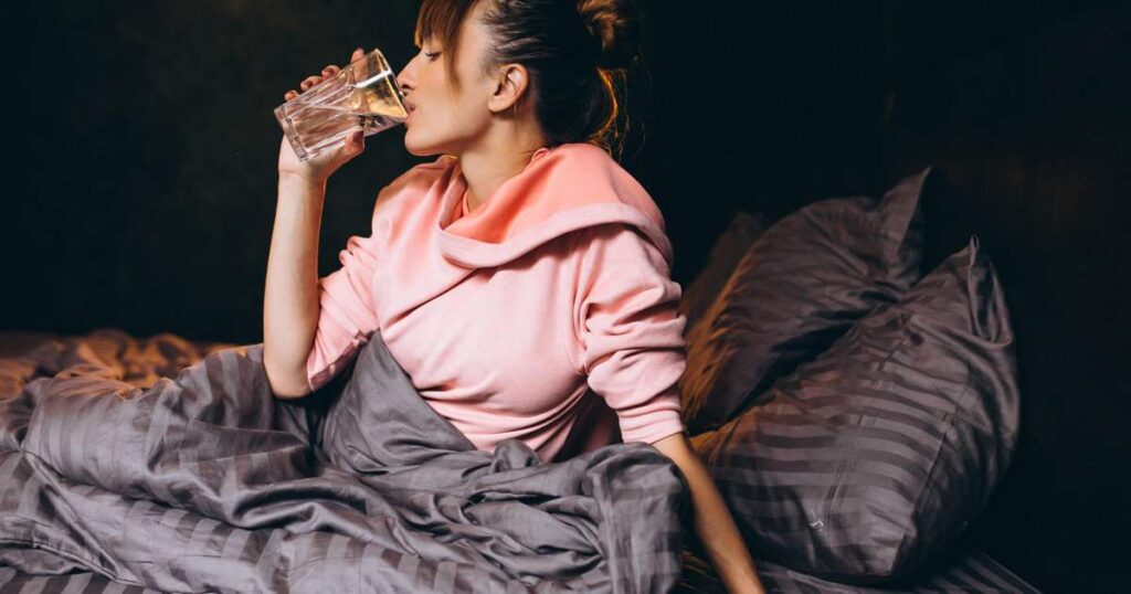 Copo de água ao lado da cama, simbolizando a hidratação noturna e seus efeitos no sono