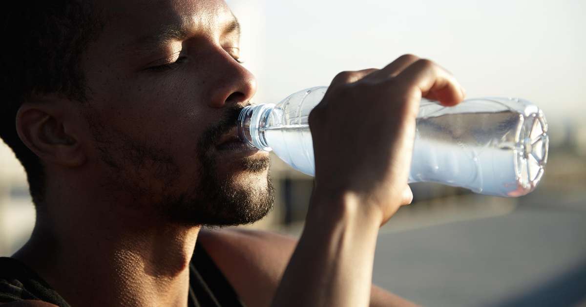 Uma pessoa bebendo água de um copo ao ar livre, simbolizando a importância da hidratação.
