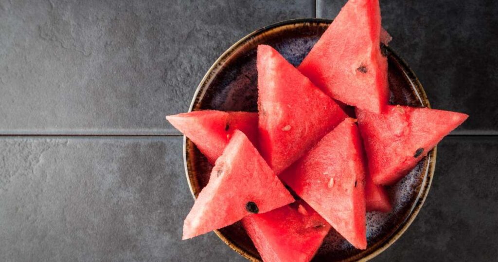 Chá de melancia em uma xícara com fatias de melancia ao fundo