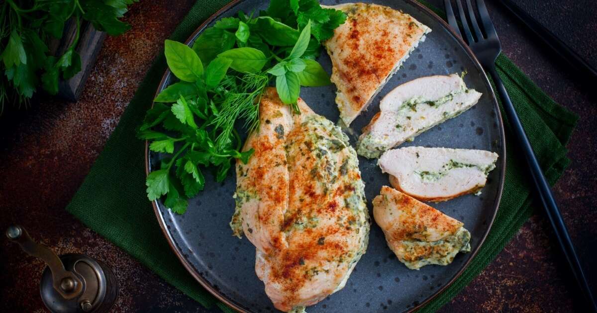 Frango cozido completamente em uma tábua de cortar com utensílios de cozinha ao fundo
