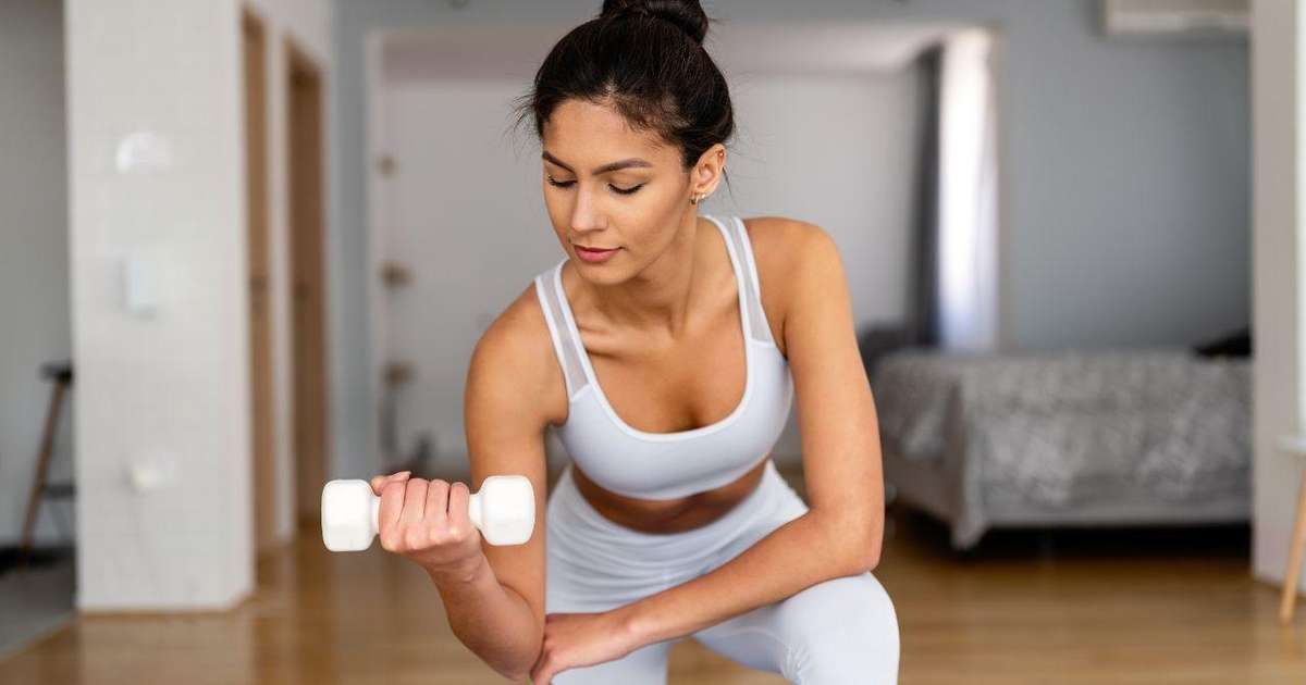 Pessoa treinando em casa com equipamentos de ginástica como halteres e colchonete