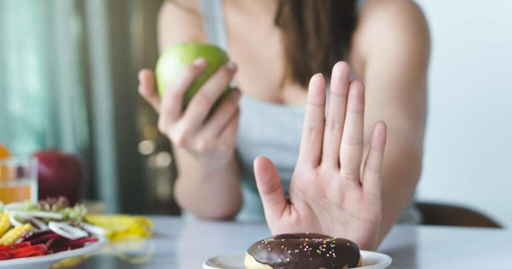 Uma pessoa segurando uma maçã enquanto olha para um prato vazio simbolizando a redução do açúcar na dieta.