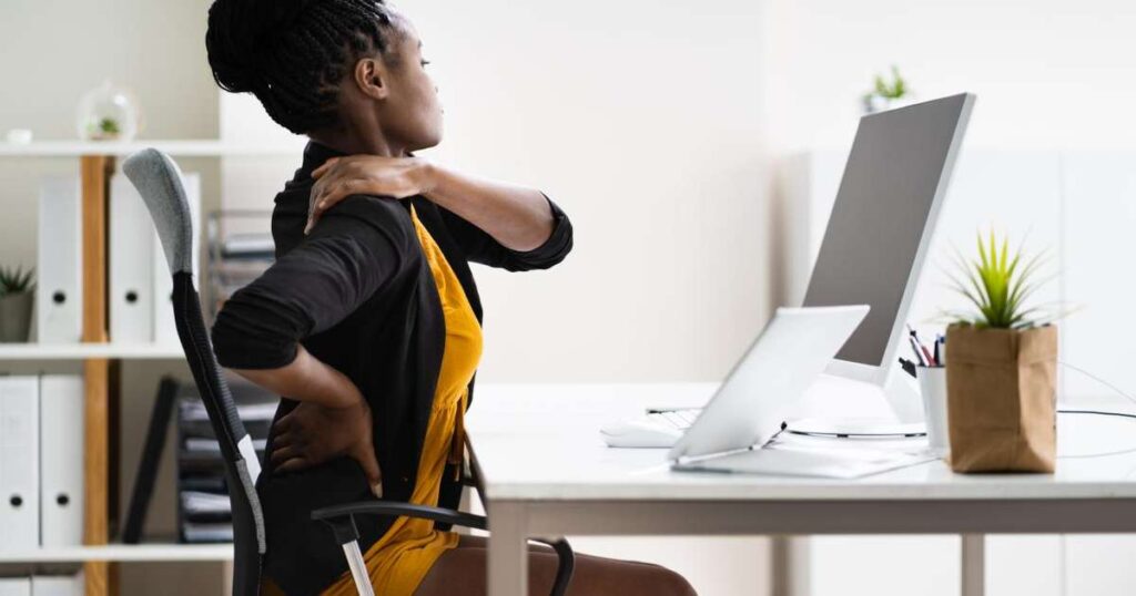 Pessoa sentada em uma cadeira com expressão de dor nas costas e glúteos, simbolizando a síndrome do piriforme.